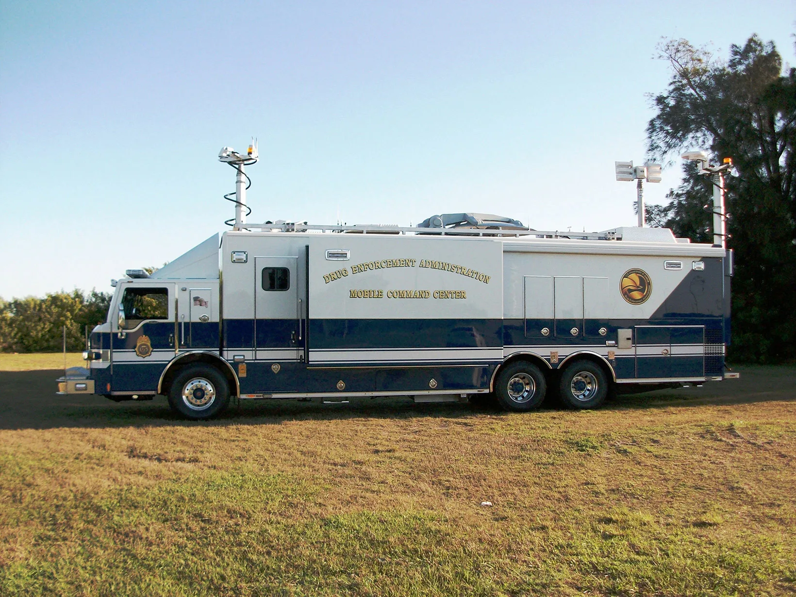 Frontline Communications DEA C-40X-3 Mobile Command Unit parked outside in the grass on a sunny day near trees.