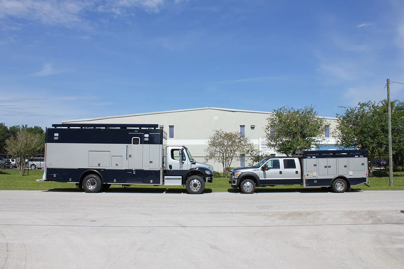 An FBI TRU Mobile Command Vehicle and Trailer parked outside near the Frontline Communications building on a sunny day.
