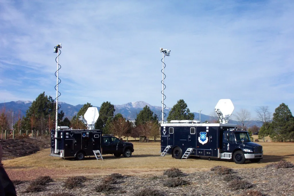 A Frontline Communications C-35 and C-25 Mobile Command Vehicle parked outside in the grass on a cloudy day.