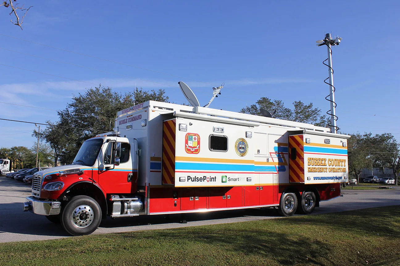 Frontline Communications C-45X-4 Emergency Operations Center vehicle for Sussex County parked outside near grass and trees on a sunny day.