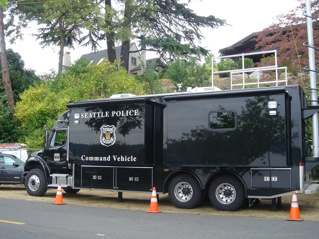 Frontline Communications black C-35X Mid-Size Mobile Command vehicle parked outside near trees on a cloudy day.