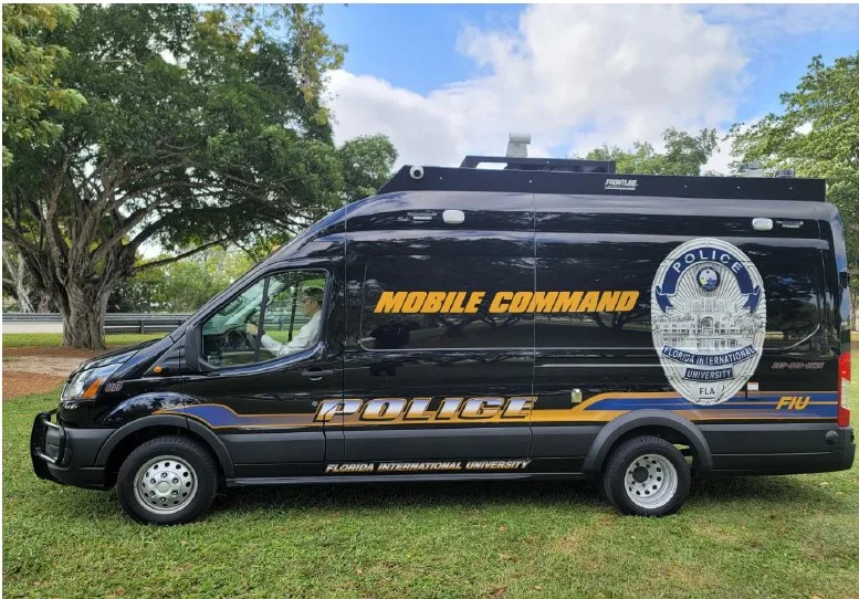 Frontline Communications FIU C-22 Small Mobile Command vehicle parked outside on the grass near trees on a cloudy day.