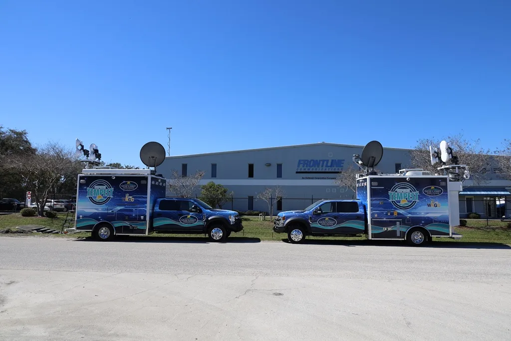 Two C-25 Small Mobile Command vehicles parked outside in front of the Frontline Communications building on a sunny day.