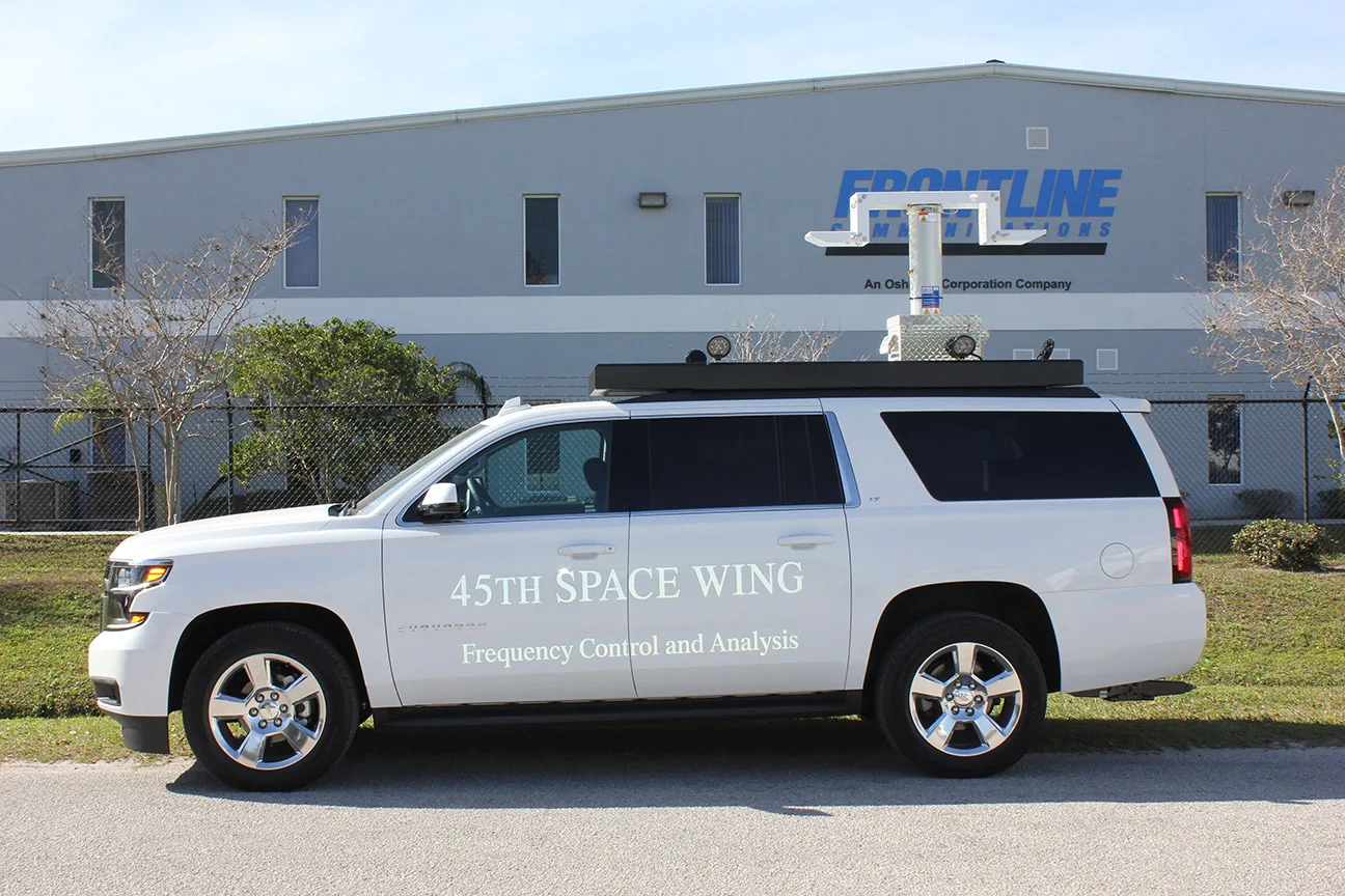 Frequency Control Analysis vehicle parked outside near the Frontline Communications building on a sunny day.