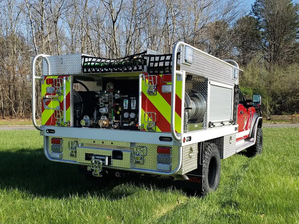 Exterior view of small fire truck showing cab, body compartments, and wheel/tire area.