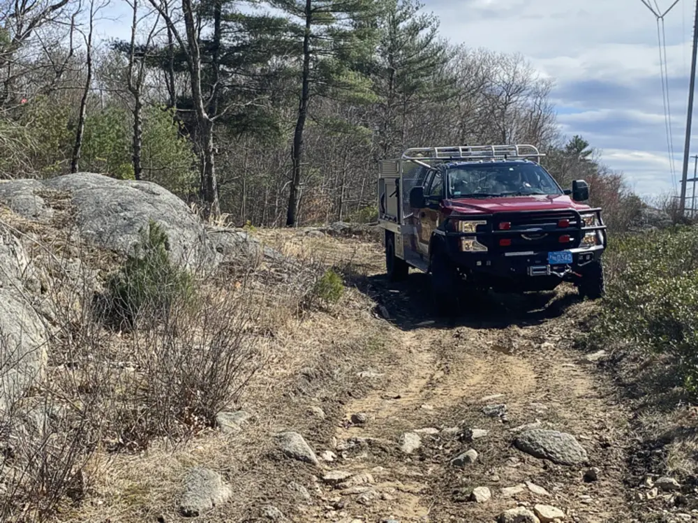 Exterior view of small fire truck showing cab, body compartments, and wheel/tire area.