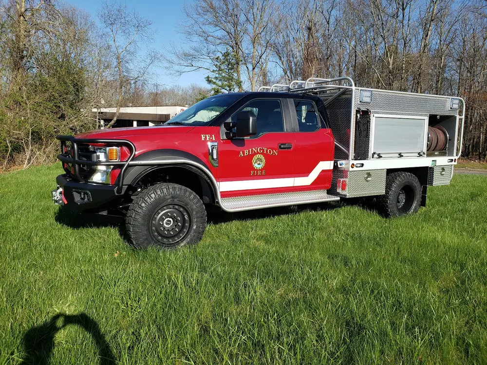 Exterior view of small fire truck showing cab, body compartments, and wheel/tire area.