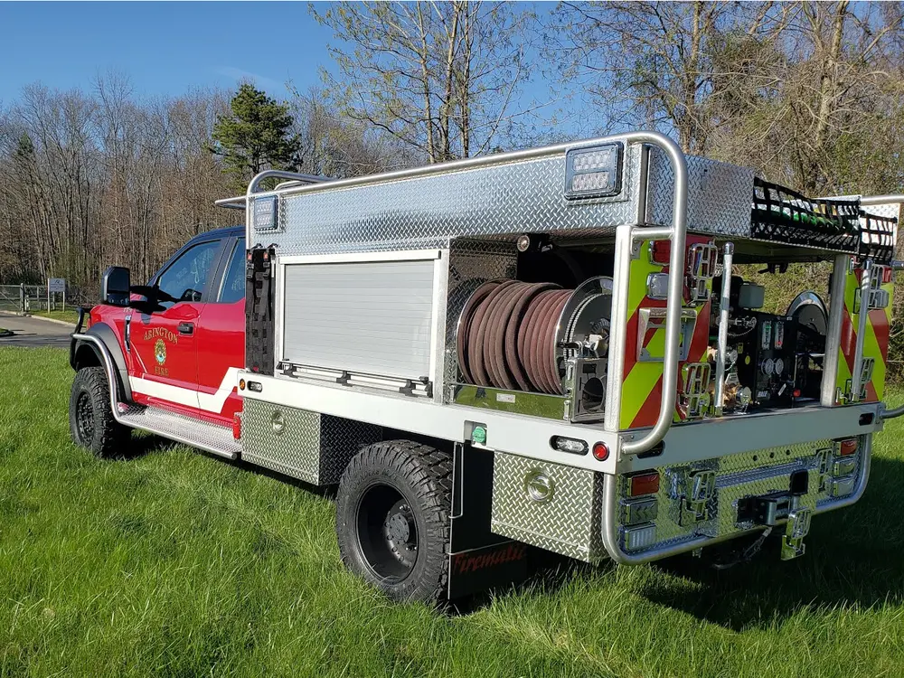 Exterior view of small fire truck showing cab, body compartments, and wheel/tire area.