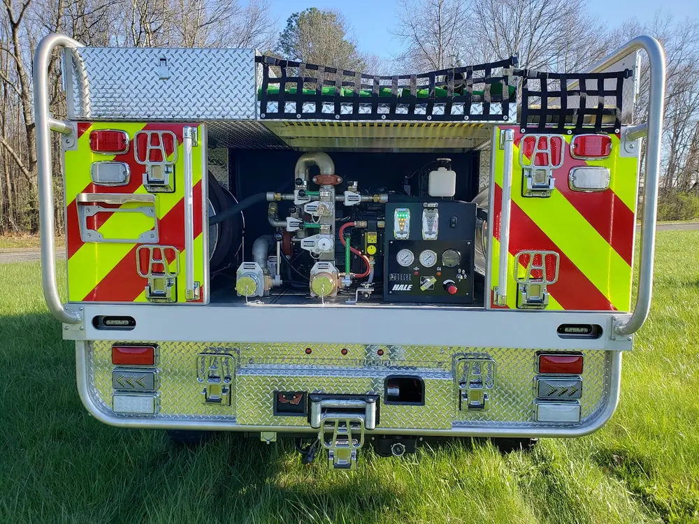Exterior view of small fire truck showing cab, body compartments, and wheel/tire area.