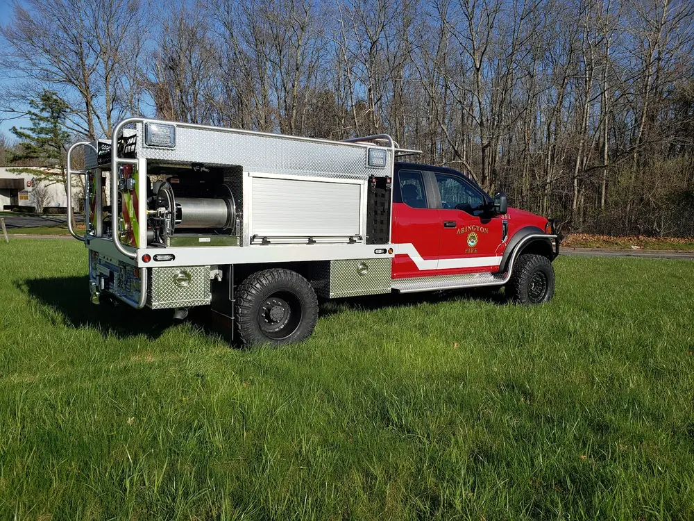 Exterior view of small fire truck showing cab, body compartments, and wheel/tire area.
