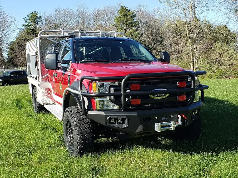 Exterior view of small fire truck showing cab, body compartments, and wheel/tire area.