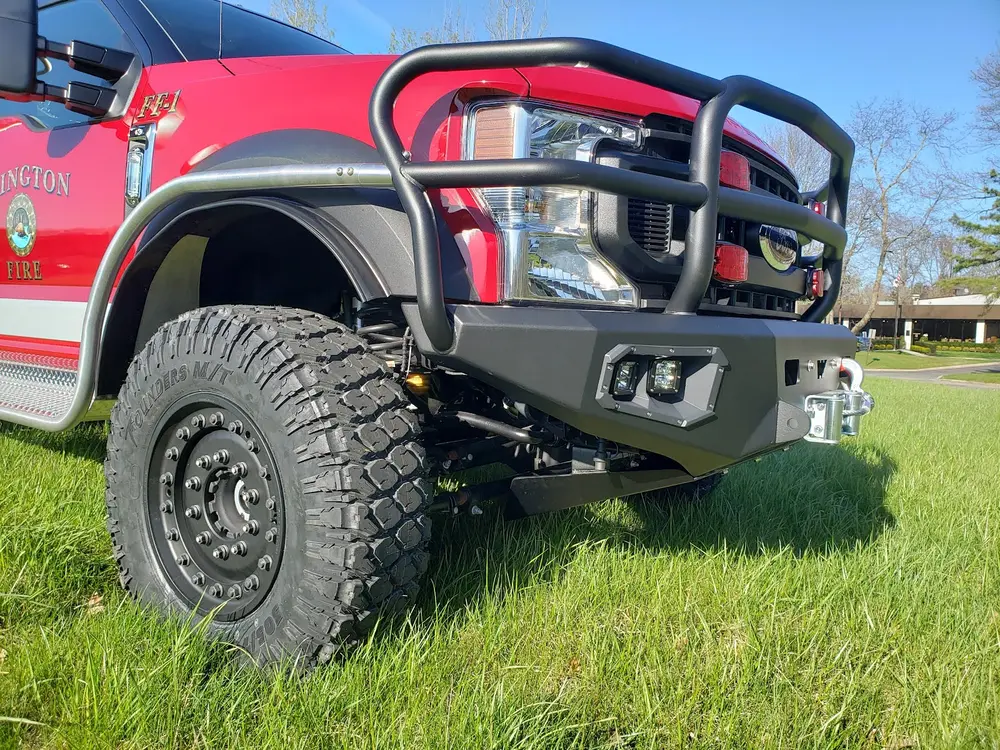 Exterior view of small fire truck showing cab, body compartments, and wheel/tire area.