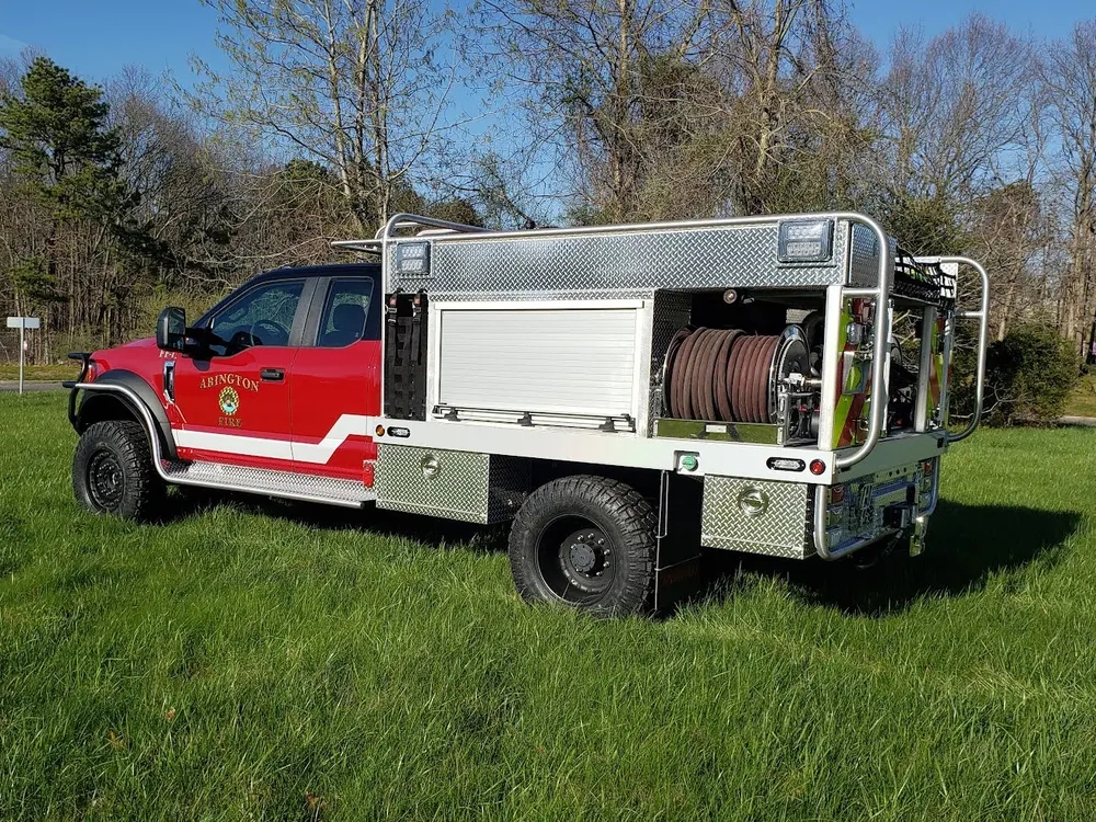 Exterior view of small fire truck showing cab, body compartments, and wheel/tire area.
