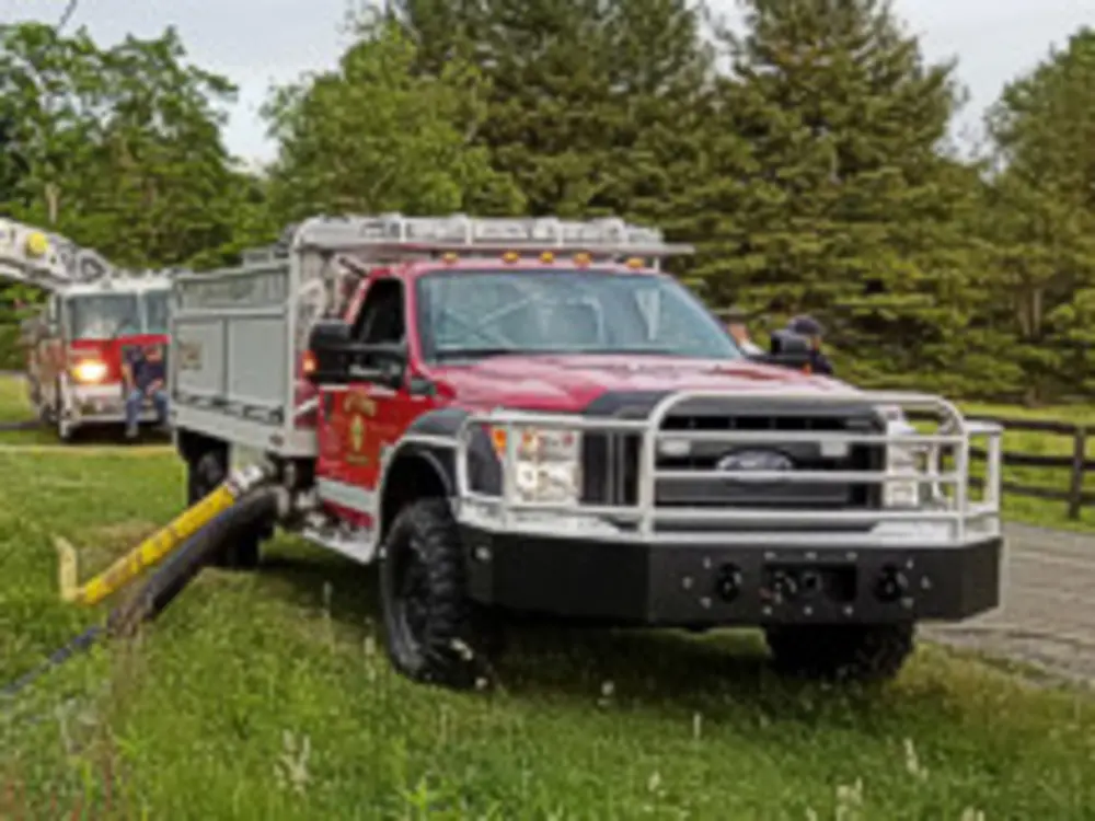 Exterior view of small fire truck showing cab, body compartments, and wheel/tire area.