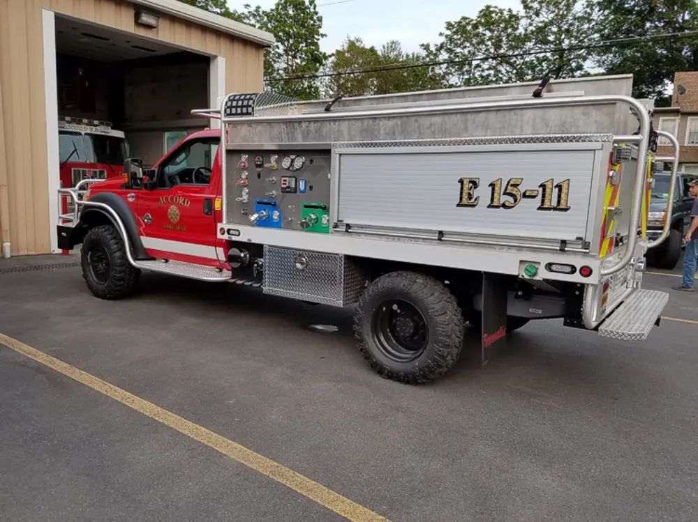 Exterior view of small fire truck showing cab, body compartments, and wheel/tire area.