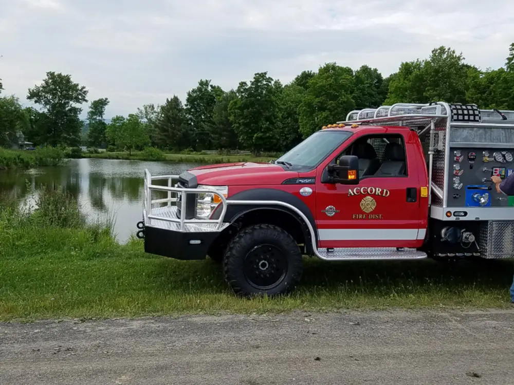 Exterior view of small fire truck showing cab, body compartments, and wheel/tire area.