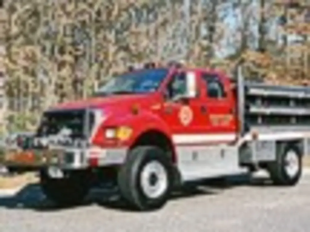 Exterior view of small fire truck showing cab, body compartments, and wheel/tire area.