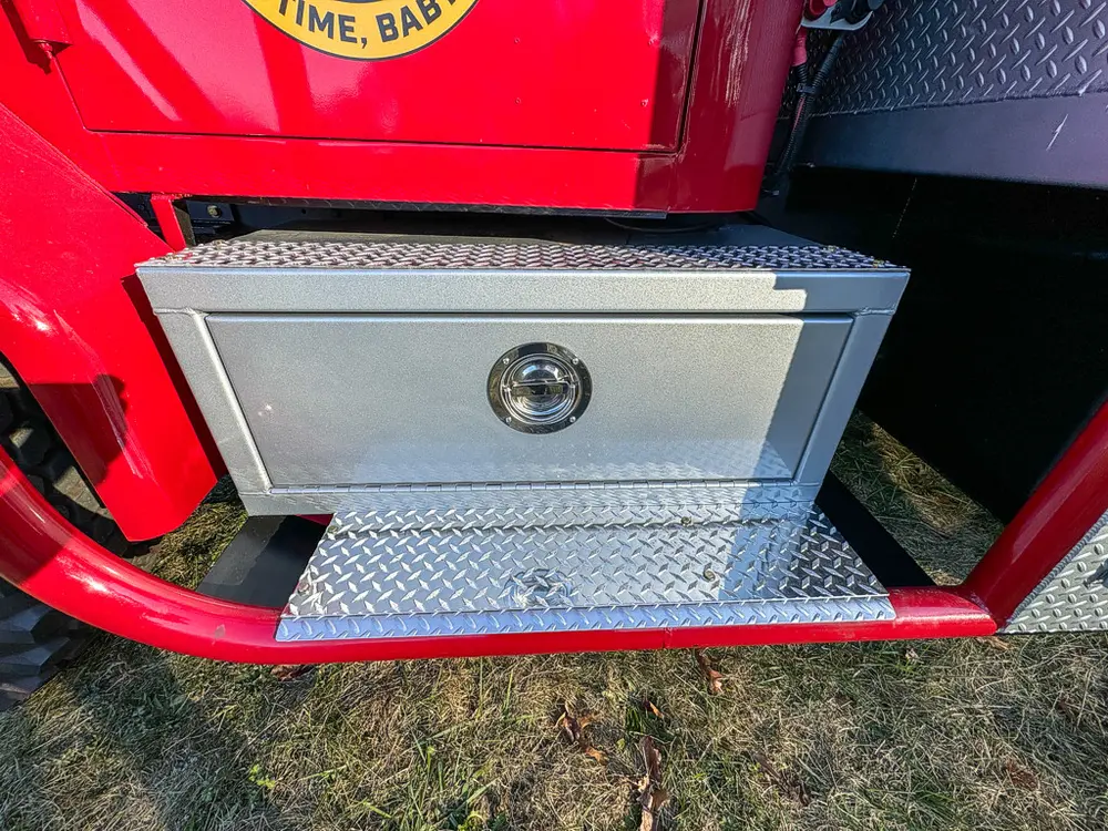 Diamond-plate side compartment door closed above the side step.