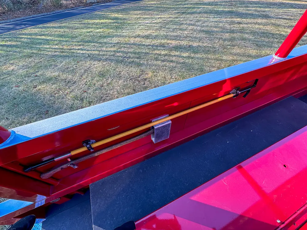 Top-side storage trough close-up with long tool secured inside.