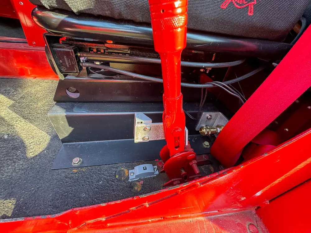Center floor close-up with red control lever and seatbelt anchor.