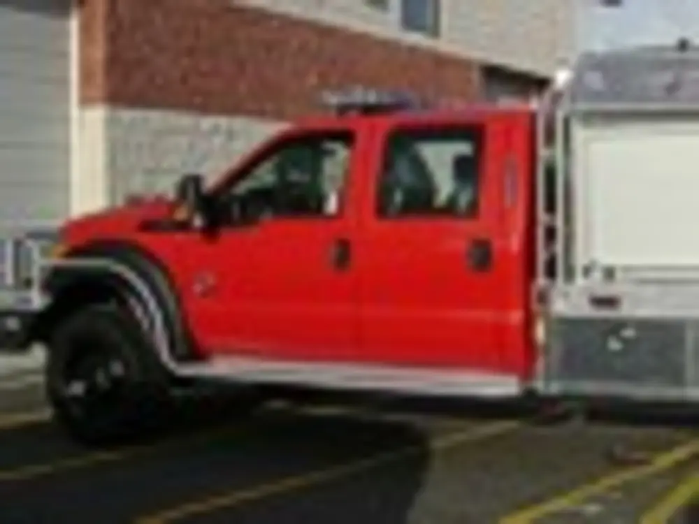 Exterior view of small fire truck showing cab, body compartments, and wheel/tire area.