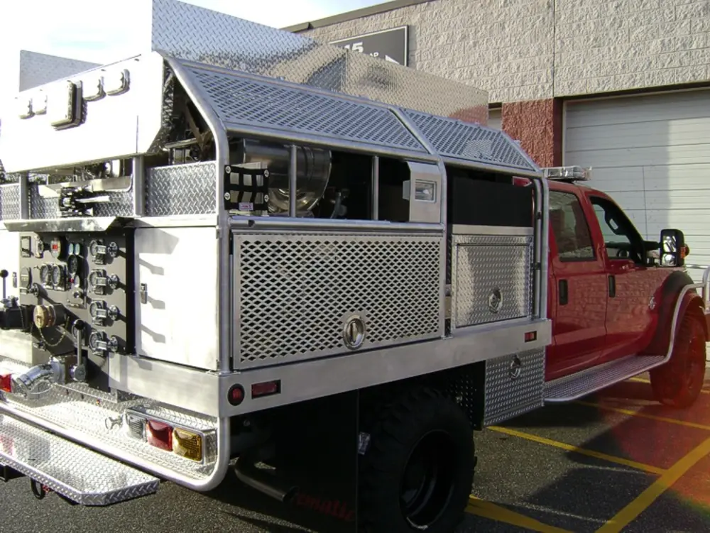 Exterior view of small fire truck showing cab, body compartments, and wheel/tire area.
