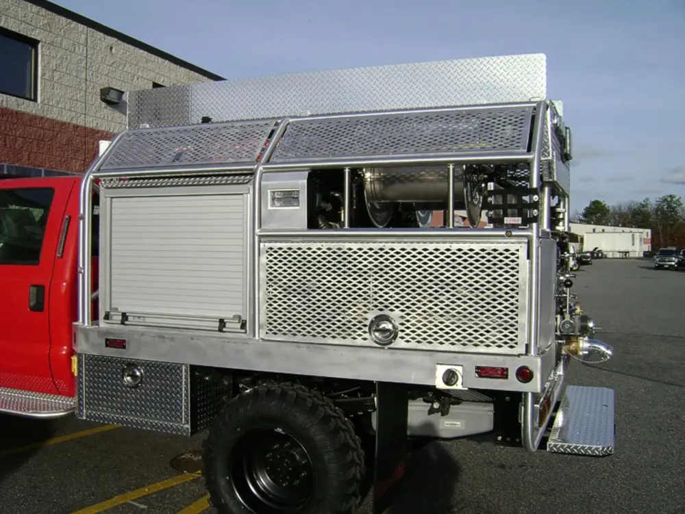 Exterior view of small fire truck showing cab, body compartments, and wheel/tire area.