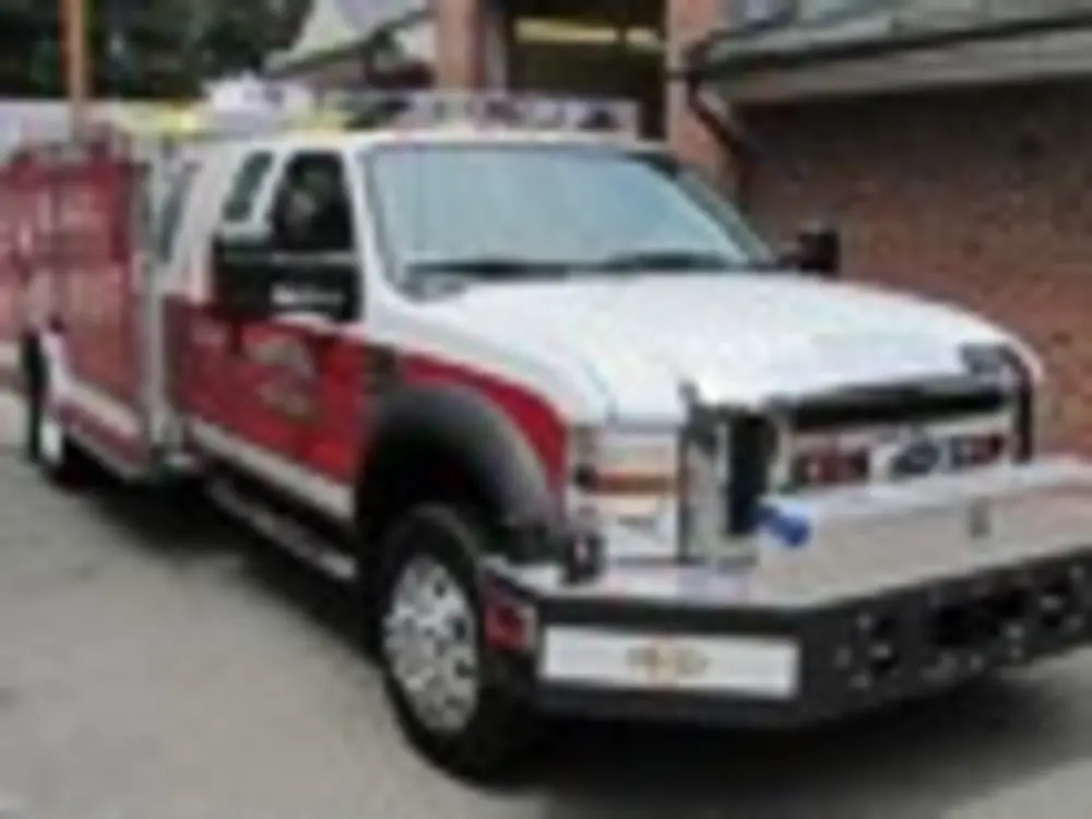 Exterior view of small fire truck showing cab, body compartments, and wheel/tire area.