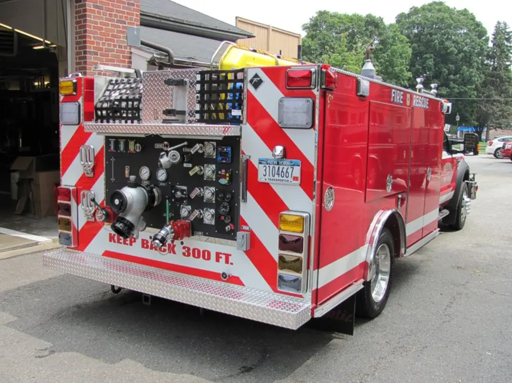 Exterior view of small fire truck showing cab, body compartments, and wheel/tire area.