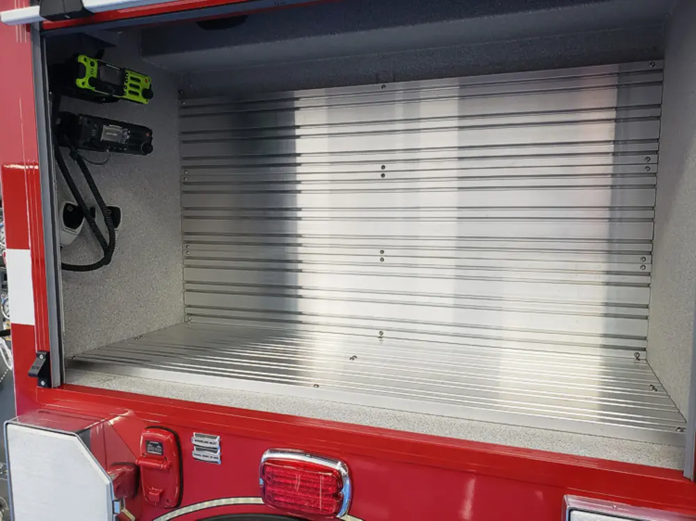 Exterior view of small fire truck showing cab, body compartments, and wheel/tire area.