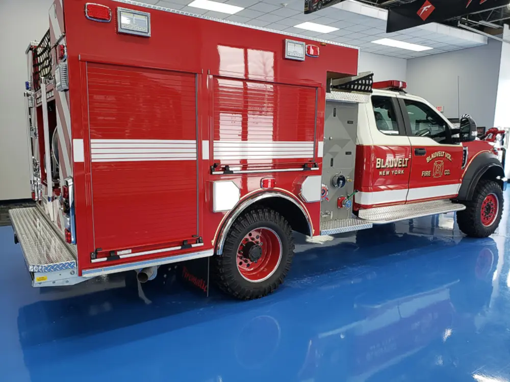 Exterior view of small fire truck showing cab, body compartments, and wheel/tire area.