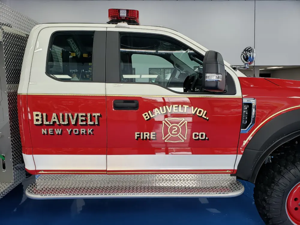 Exterior view of small fire truck showing cab, body compartments, and wheel/tire area.