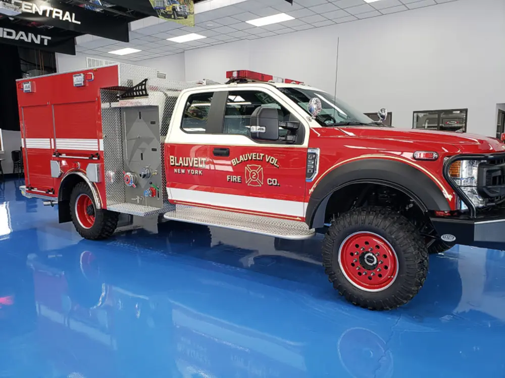 Exterior view of small fire truck showing cab, body compartments, and wheel/tire area.