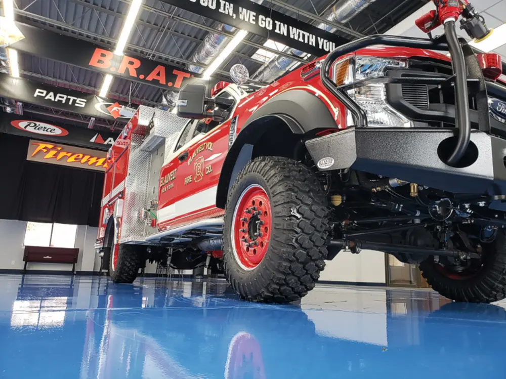 Exterior view of small fire truck showing cab, body compartments, and wheel/tire area.