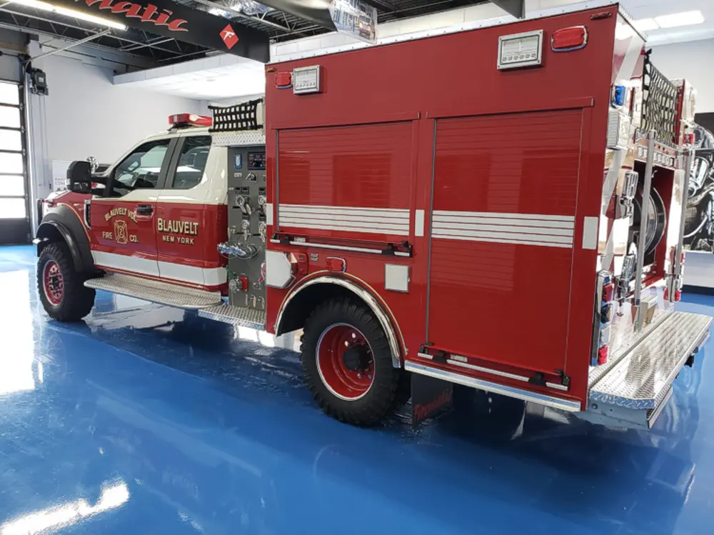 Exterior view of small fire truck showing cab, body compartments, and wheel/tire area.