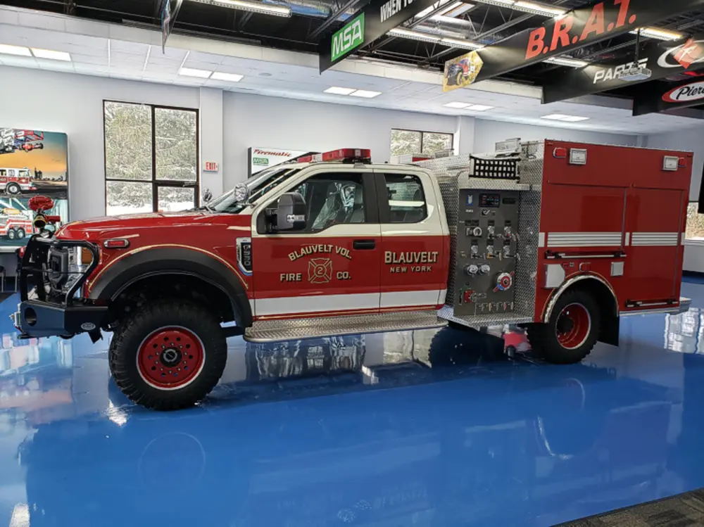 Exterior view of small fire truck showing cab, body compartments, and wheel/tire area.