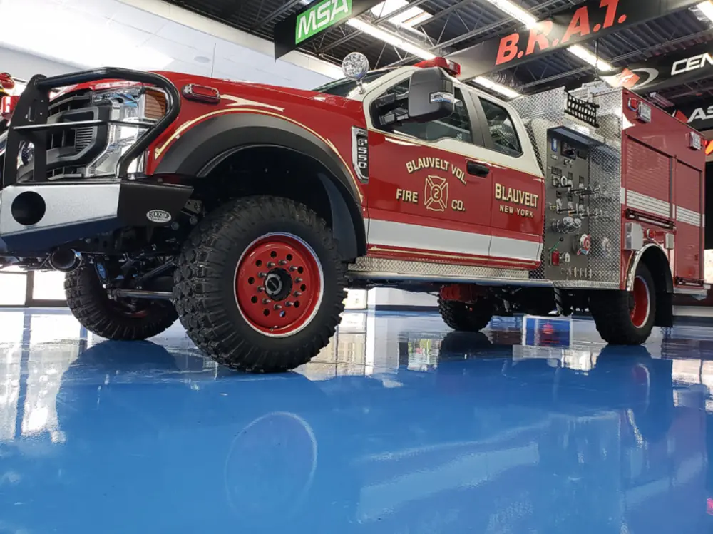 Exterior view of small fire truck showing cab, body compartments, and wheel/tire area.