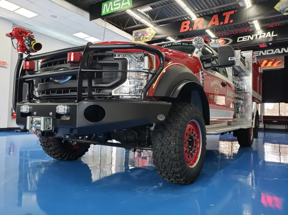 Exterior view of small fire truck showing cab, body compartments, and wheel/tire area.