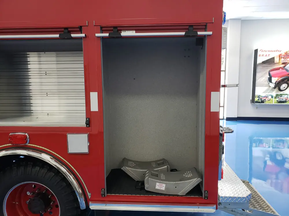 Exterior view of small fire truck showing cab, body compartments, and wheel/tire area.