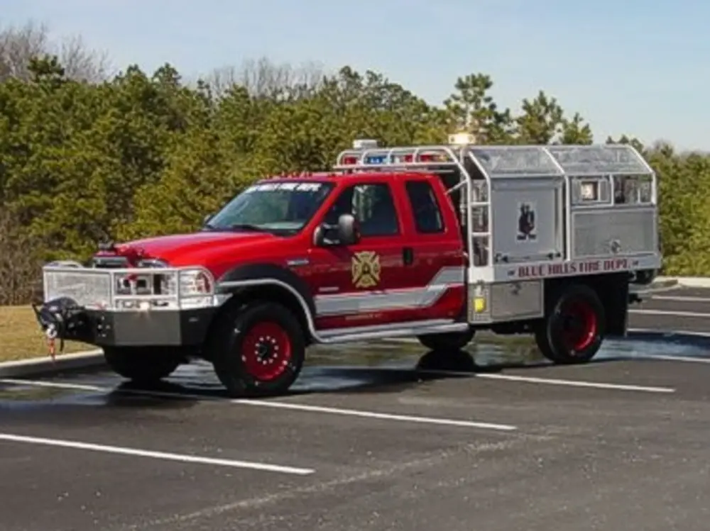 Exterior view of small fire truck showing cab, body compartments, and wheel/tire area.
