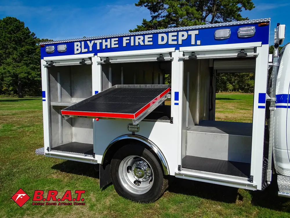 Exterior view of small fire truck showing cab, body compartments, and wheel/tire area.