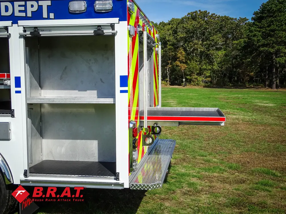 Exterior view of small fire truck showing cab, body compartments, and wheel/tire area.