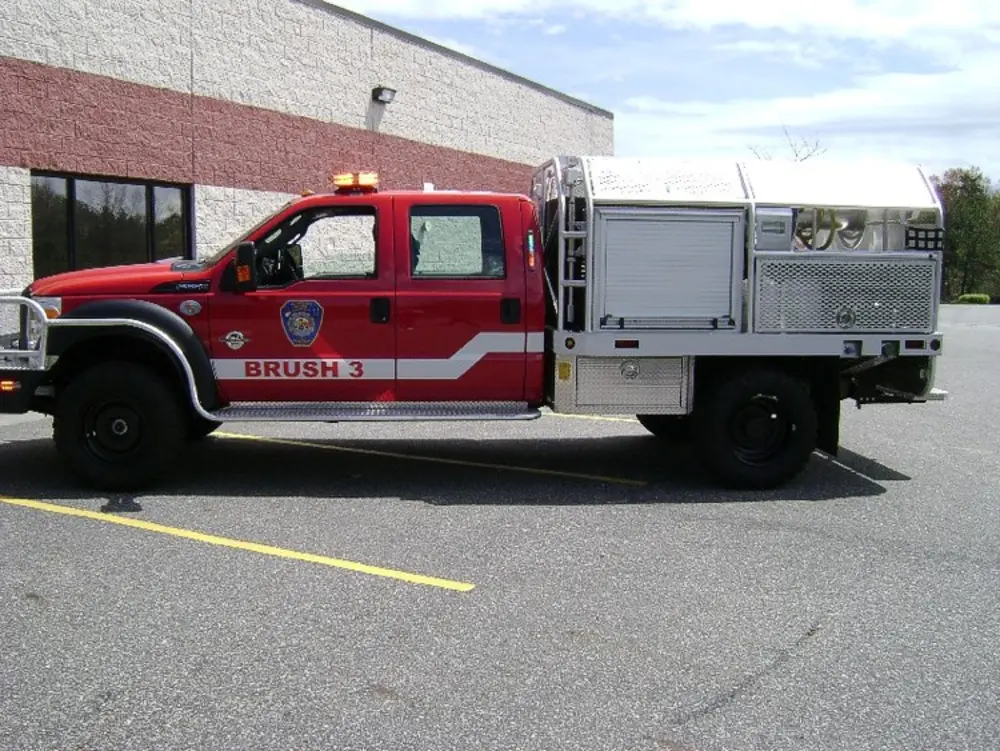 Exterior view of small fire truck showing cab, body compartments, and wheel/tire area.
