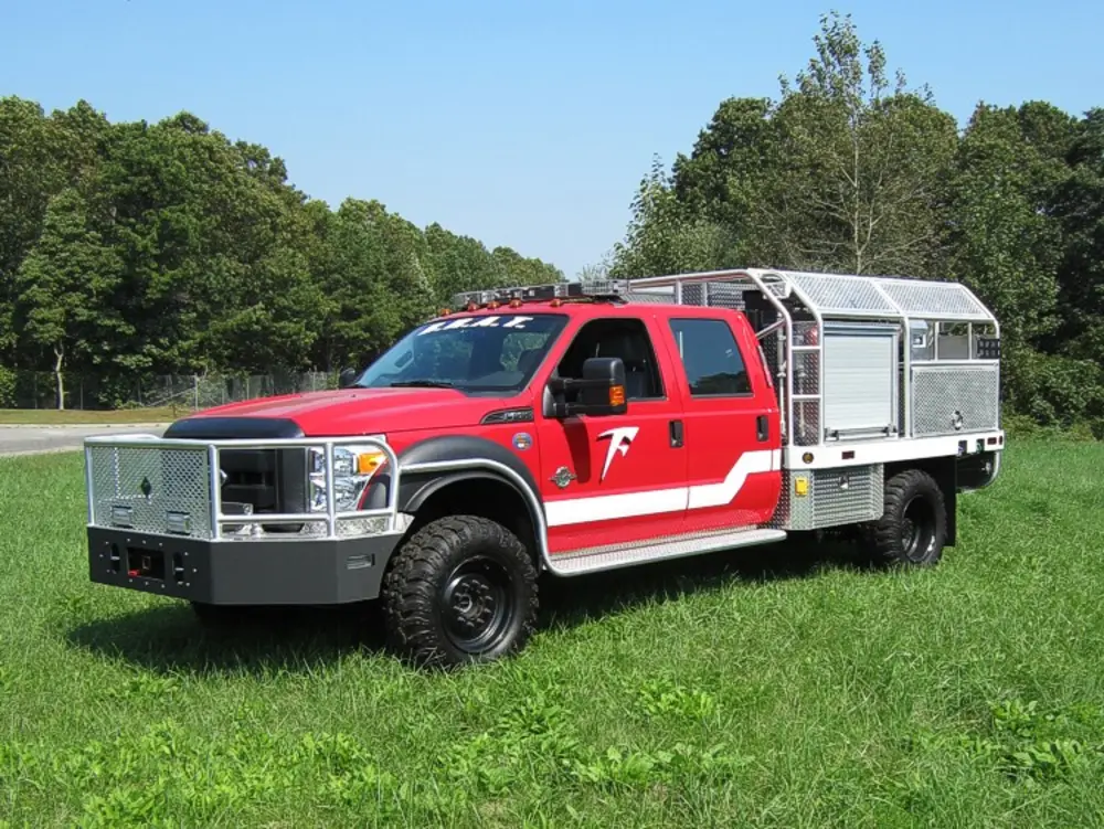 Exterior view of small fire truck showing cab, body compartments, and wheel/tire area.