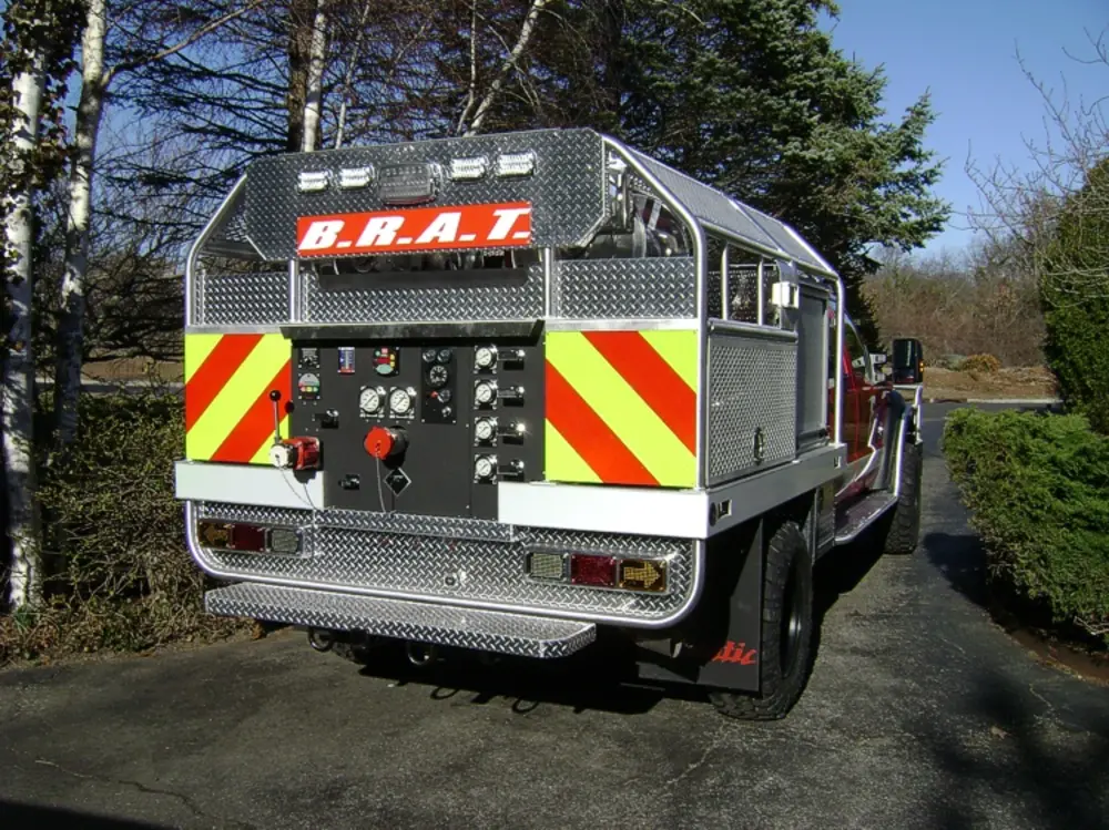 Exterior view of small fire truck showing cab, body compartments, and wheel/tire area.