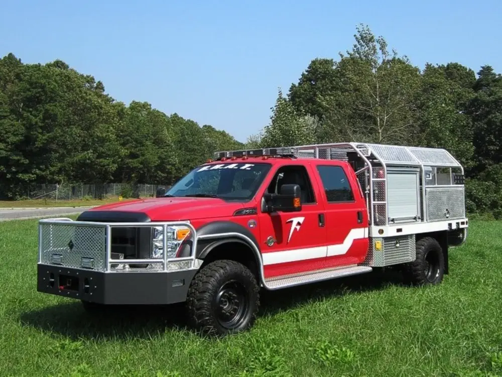 Exterior view of small fire truck showing cab, body compartments, and wheel/tire area.