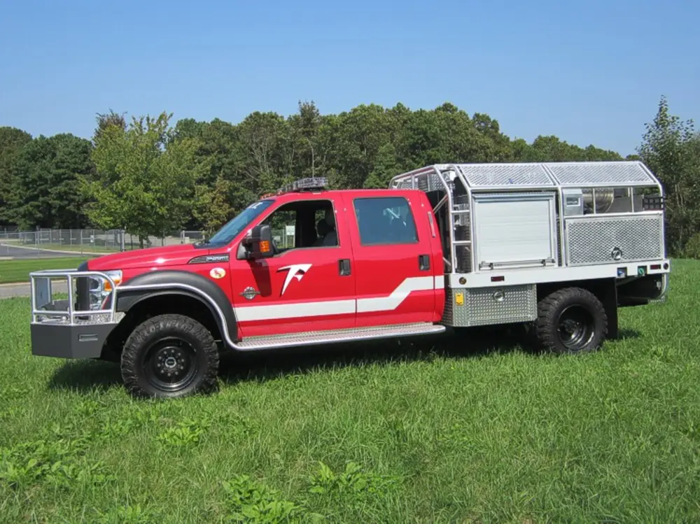 Exterior view of small fire truck showing cab, body compartments, and wheel/tire area.