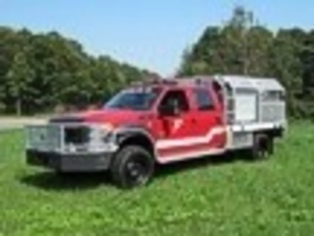 Exterior view of small fire truck showing cab, body compartments, and wheel/tire area.