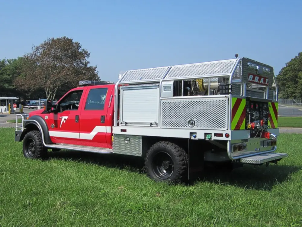 Exterior view of small fire truck showing cab, body compartments, and wheel/tire area.