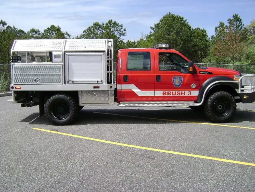 Exterior view of small fire truck showing cab, body compartments, and wheel/tire area.